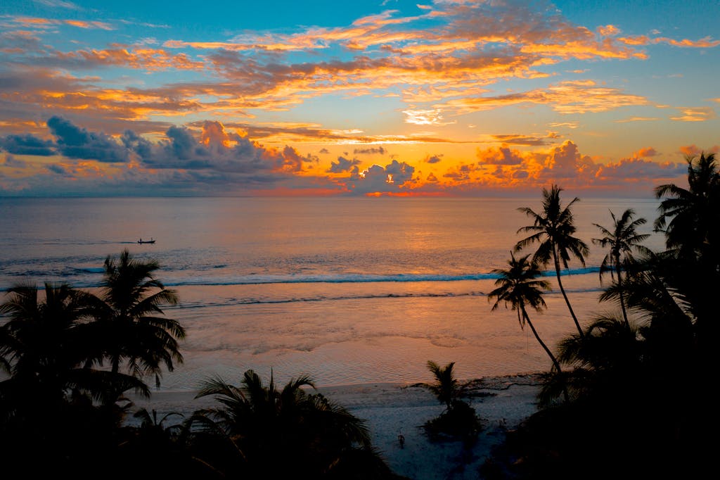 A stunning tropical sunset over a tranquil ocean with silhouetted palm trees.