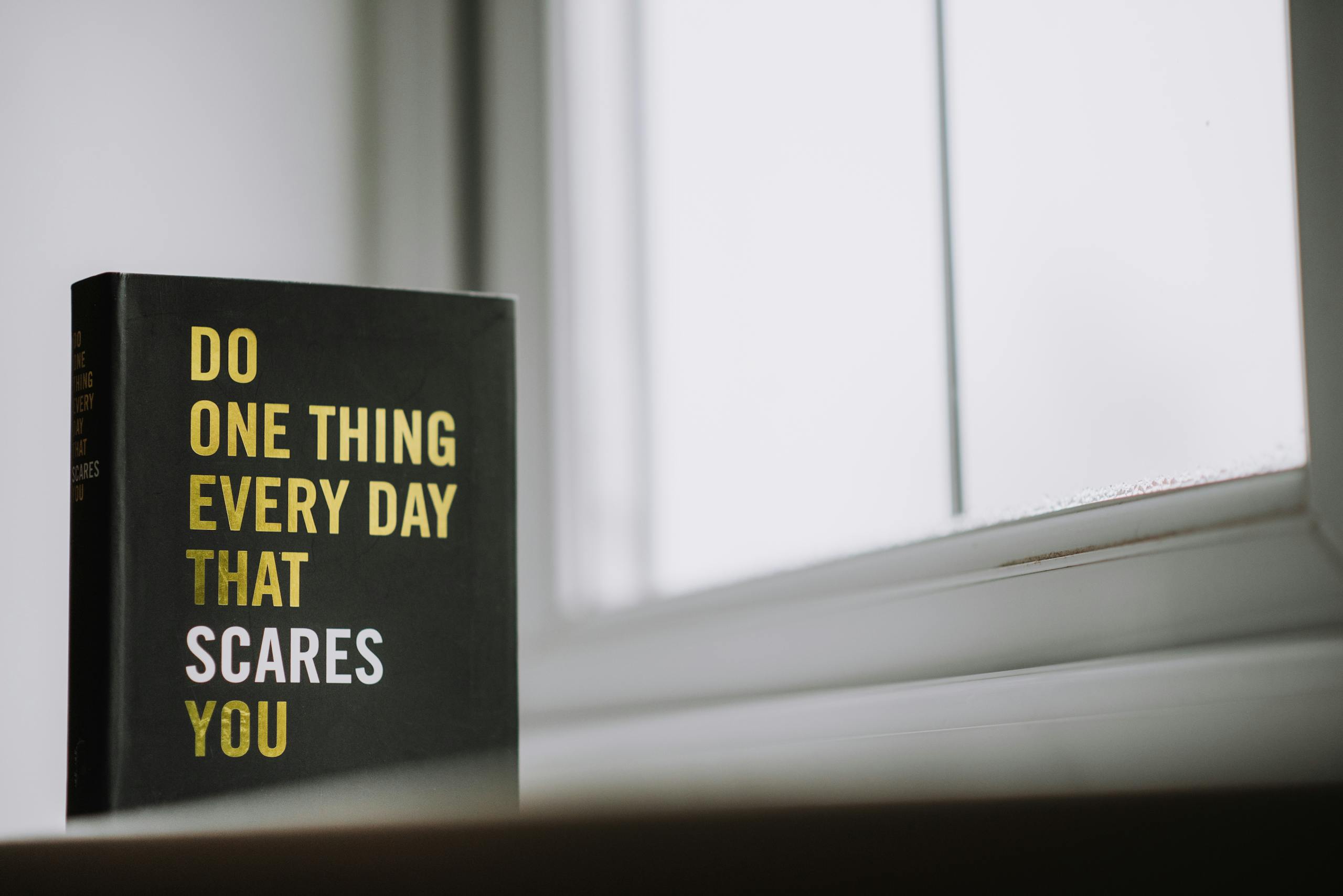 Rectangular shaped book with printed title on black hardcover on windowsill in house in daytime